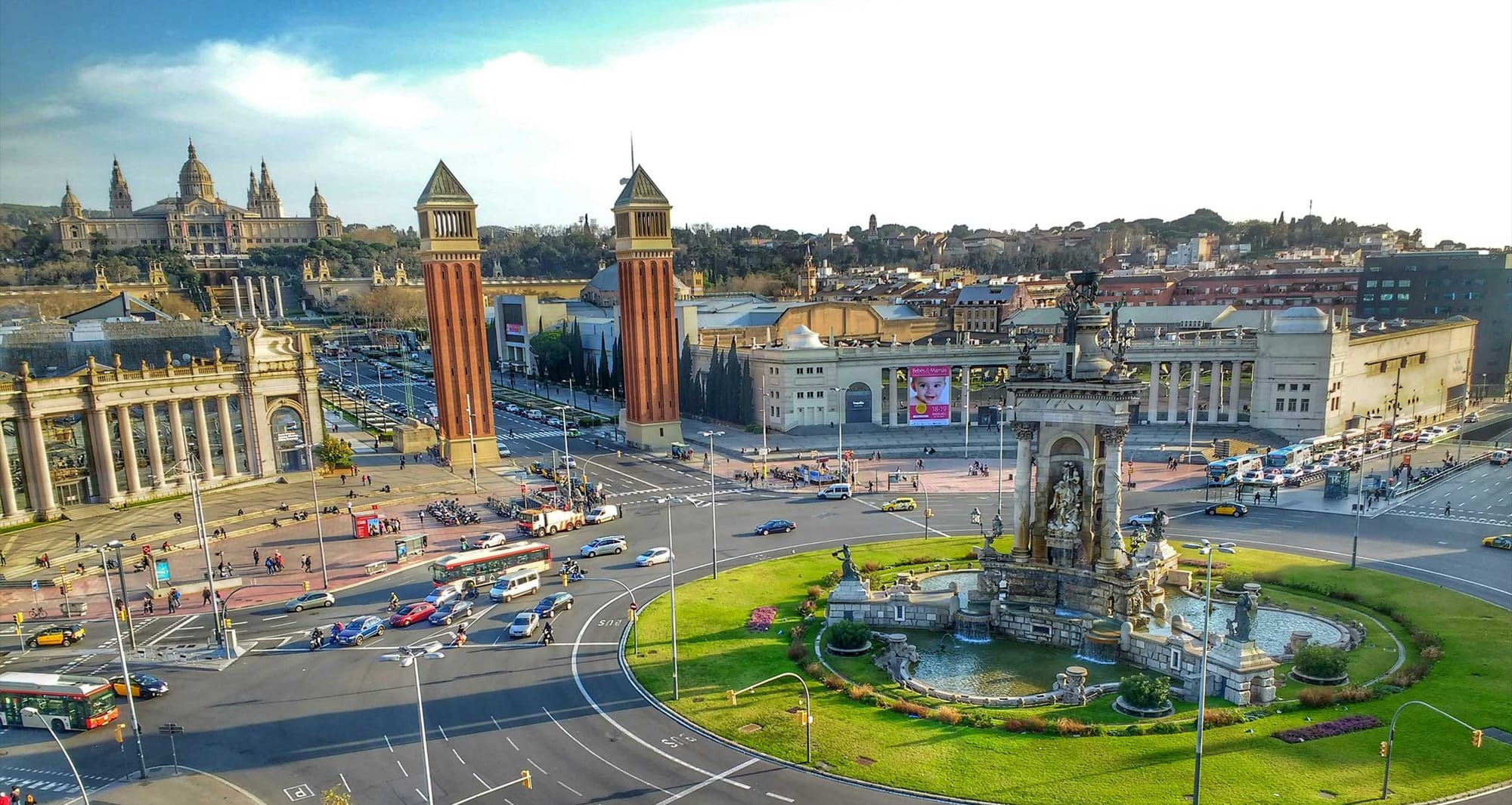 Large roundabout with a towering water fountain in Barcelona, Spain with several attractions in the background.