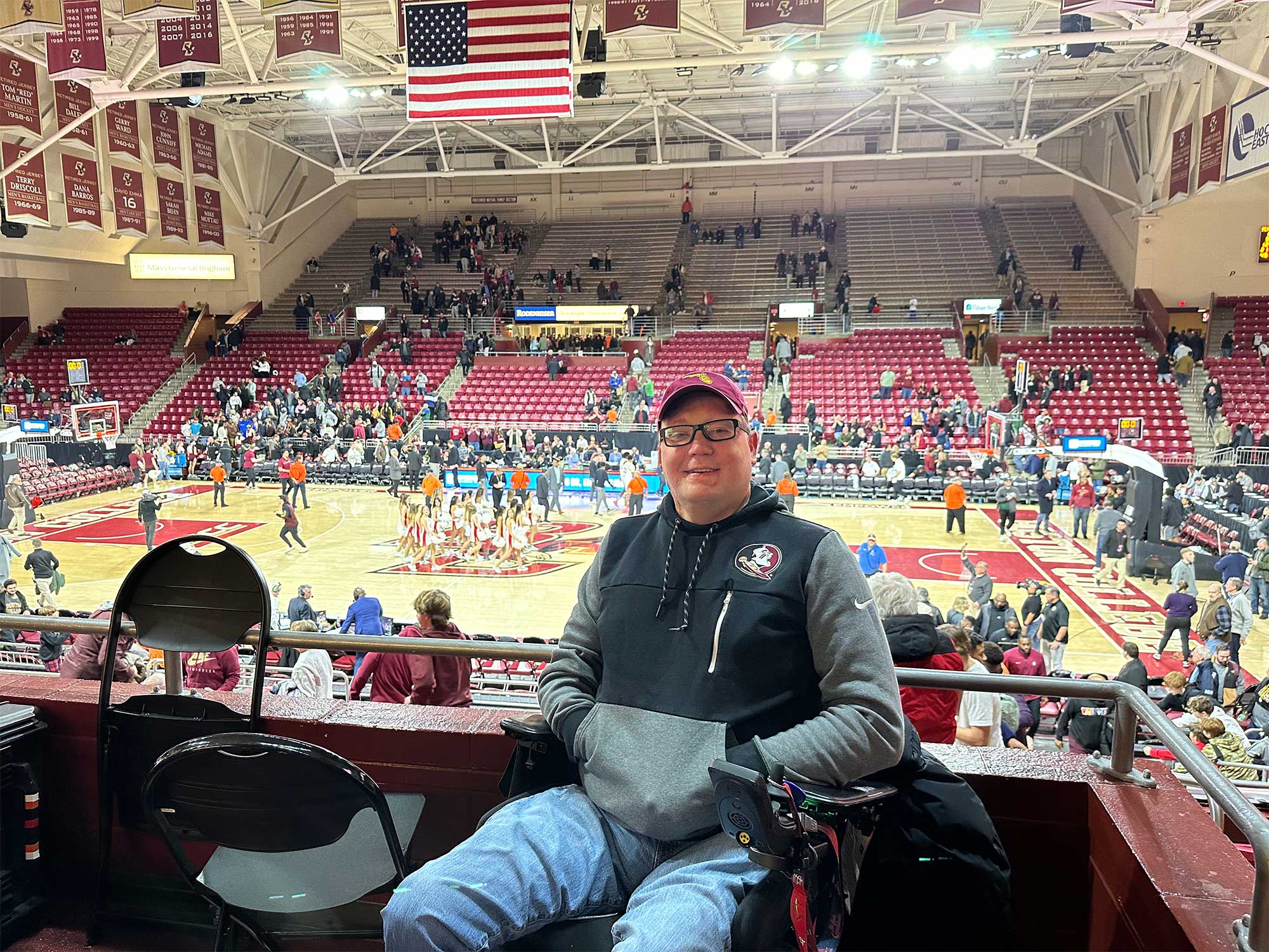 John seated in front of a basketball court at Boston College.