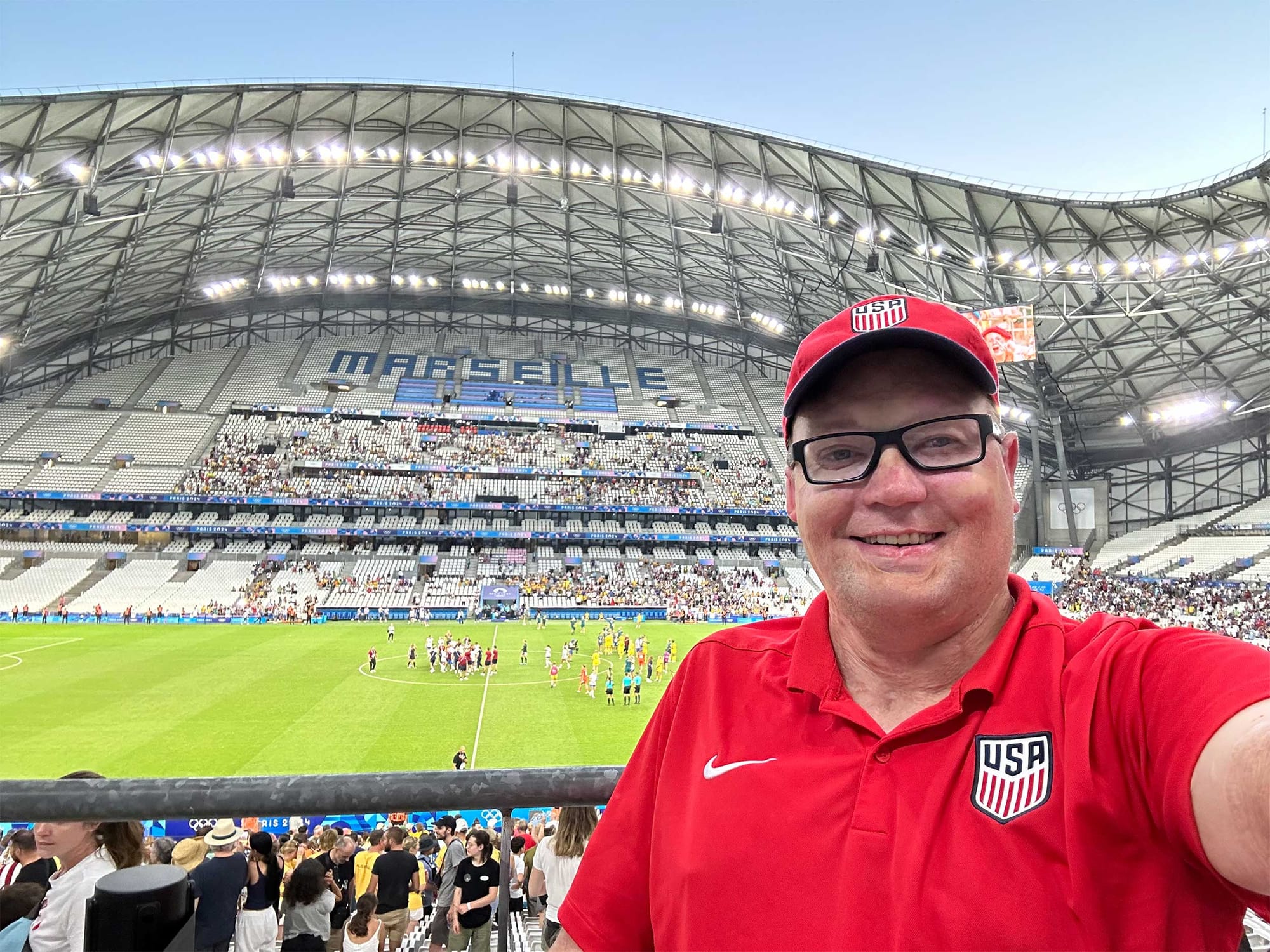 Selfie inside football stadium taken after match, John is wearing a red Team USA polo shirt.