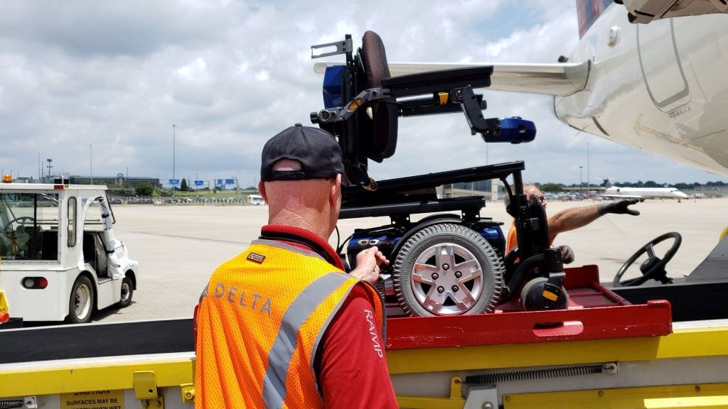 Power wheelchair being loaded by staff members onto Delta airplane.