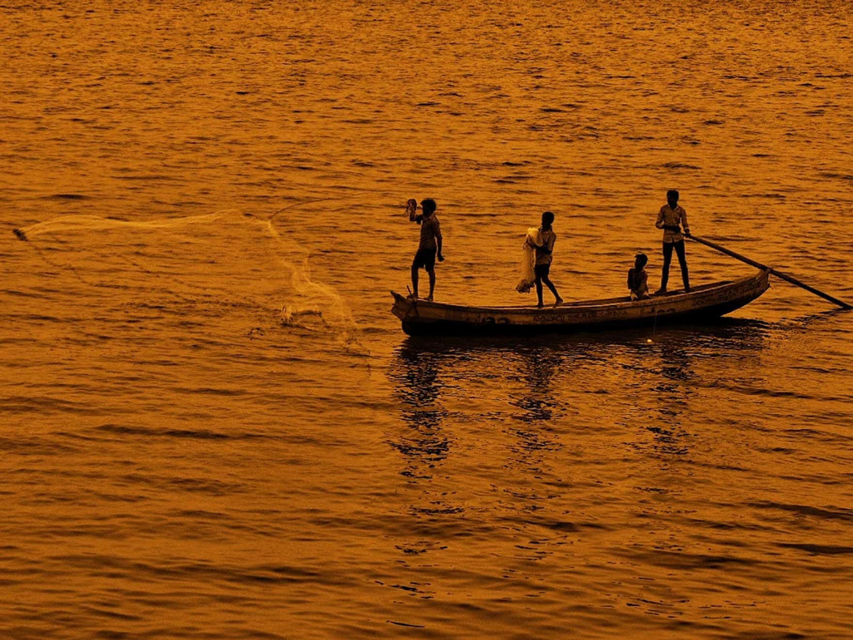 Fishermen casting their nets in the twilight glow of the Godavari River, with the bridge elegantly silhouetted in the background