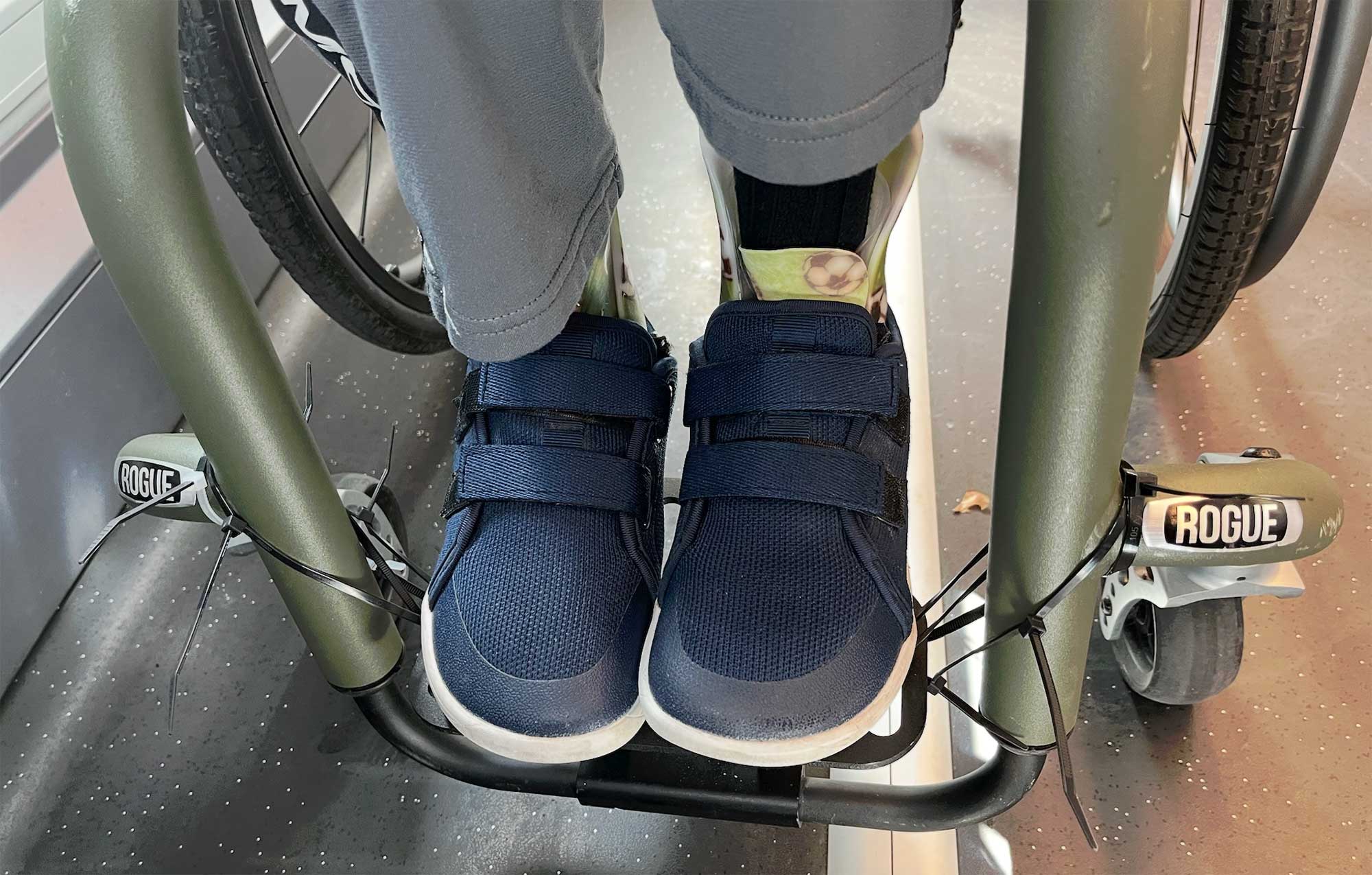 Close up of feet on a manual wheelchair, with zip ties holding the foot plate to the frame.