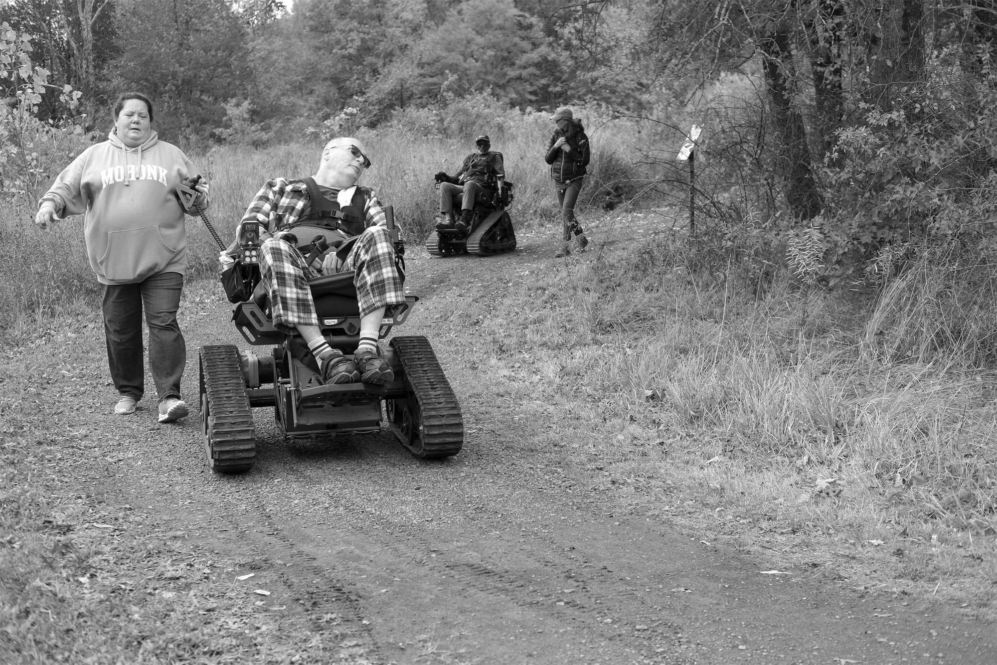 People using track chairs on an outdoor trail.