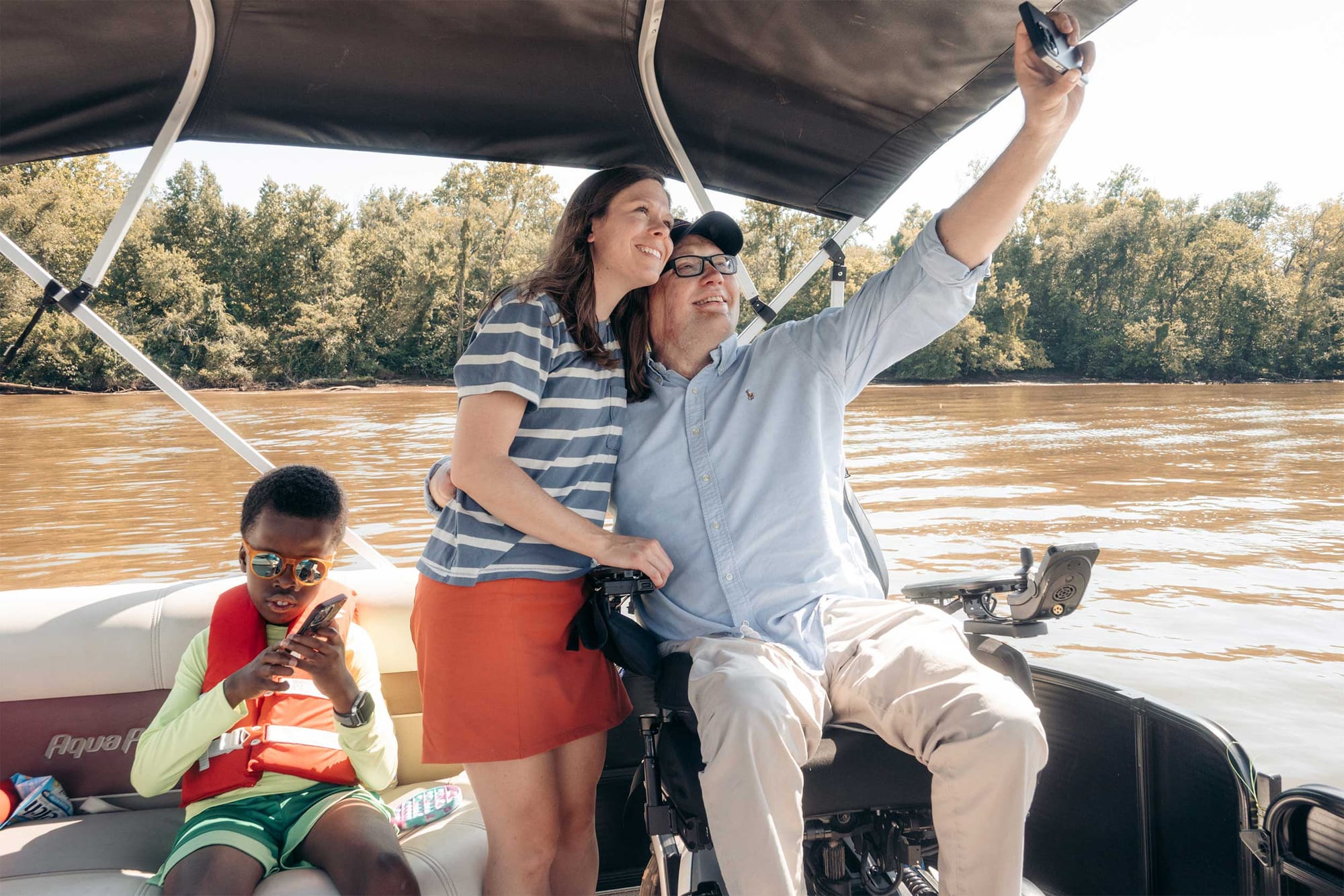 John and Stevie taking a selfie on a boat, with Robert in the background.