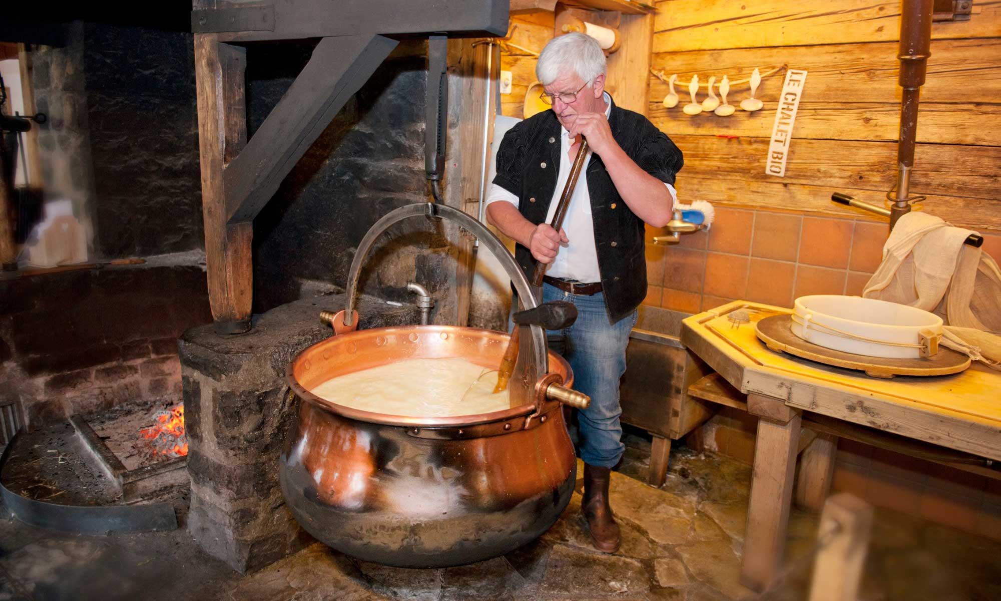 Man tending to cheese heated in a copper cauldron.