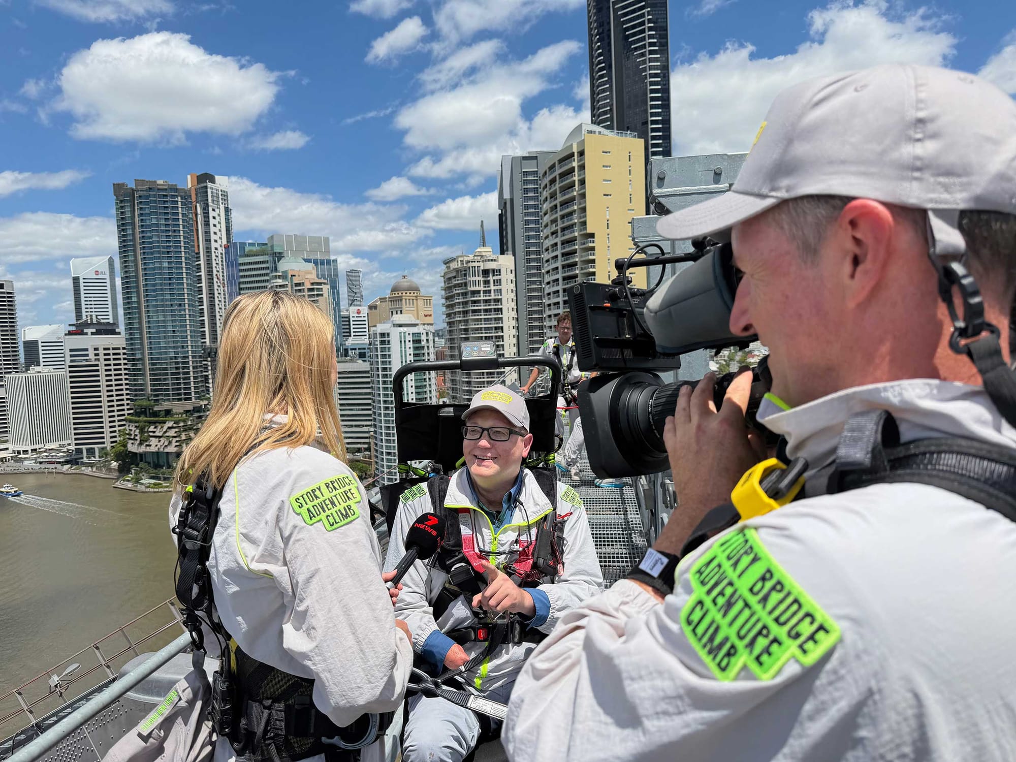 Television journalist with cameraman interviewing John at the top of a bridge.