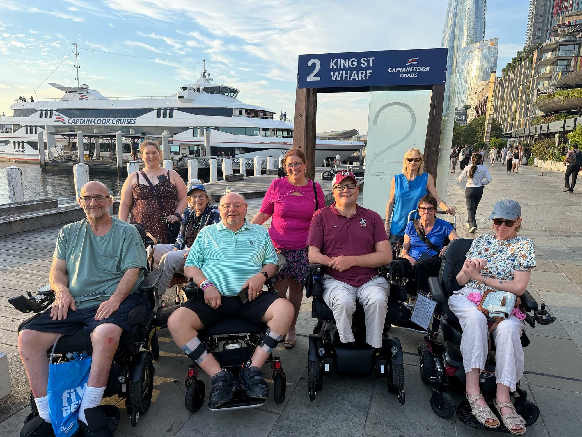 John pictured with a group of wheelchair users and their companions in front of a sightseeing cruise ship in Sydney's King Street Wharf.