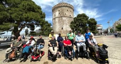 Group of wheelchair and scooter users in front of White Tower in Thessaloniki, Greece.