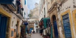 Moroccan street with shops, colorful doors and a fortified building in the distance with a tower above the city.
