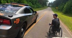 Wheelchair user on street next to a highway patrol car.