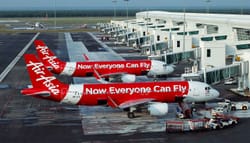 PHOTO DESCRIPTION: Two AirAsia jets at airport terminal, with a livery that says on the side of the plane, 'Now everyone can