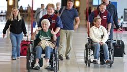 Passengers with reduced mobility being pushed in wheelchairs at the airport.