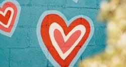 Colorful hearts painted on a cement block wall.