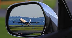 Airplane landing, reflection seen in a car's driver side mirror.