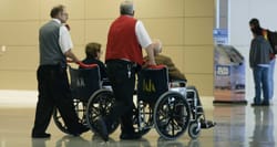 Two airline staff members pushing wheelchairs through the airport terminal.