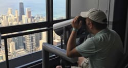 Wheelchair user looking through an accessible viewfinder towards a city skyline.