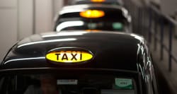 Row of black wheelchair accessible cans with a yellow taxi badge on the rooftop.