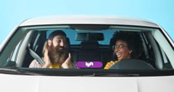 Man and woman in a white car with a illuminated Lyft sign in the window.