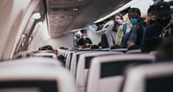 People walking down aisle of airplane wearing face masks.