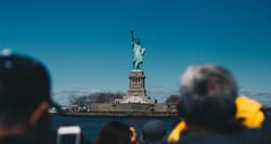 Crowd of people looking at and taking photos of the Statue of Liberty, seen on an island in the distance.