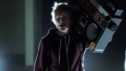 Ed Sheeran holding a large boom box over his shoulder.