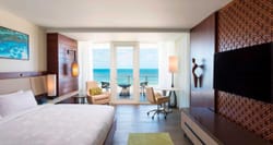 Hotel room with king size bed, wood floors and windows that look out over an oceanfront balcony.