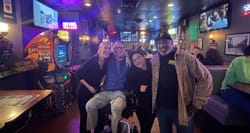 John seated in his wheelchair next to two women and a security guard at a pub.