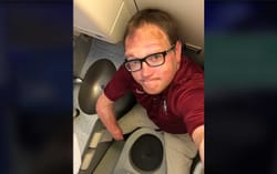 John seated on an aisle chair inside a standard sized lavatory.