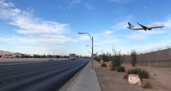 Airplane landing over roadway and sidewalk.