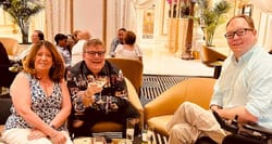 John seated with two friends, male and female, at a lounge area with multiple drinks on a table.