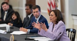 Kamala Harris speaking while seated at a table next to the Transportation Secretary.