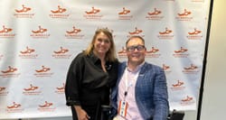 John with All Wheels Up founder Michele Erwin in front of logo banner.