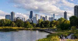 Chicago skyline pictured from a nearby public park with a lake, greenery and trails.