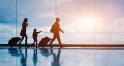 Three passengers of different sizes and ages walking through an airport terminal with luggage.