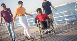 Young black wheelchair user with his friends on a boardwalk near the ocean.