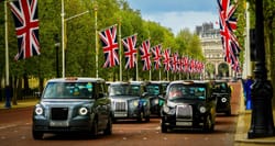 London cabs driving down a street lined with British flags.