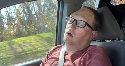 John asleep, with mouth open, in the front passenger seat of a mini van.