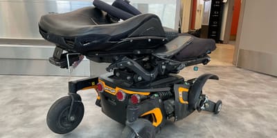 Destroyed power wheelchair with bent frame, detached drive wheel and bent armrest.