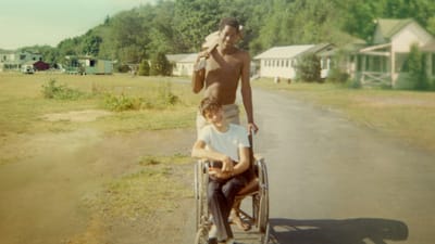 Man pushing woman in wheelchair down path at summer camp.