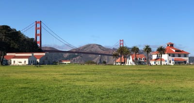 Green grassy field and historic buildings with Golden Gate Bridge in the background.