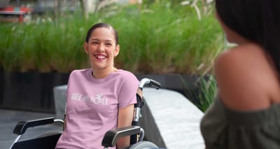 Woman sitting in wheelchair wearing a pink See Me Roll t-shirt.