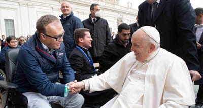 John seated in his power wheelchair shaking hands with Pope Francis, who is seated in a manual wheelchair.