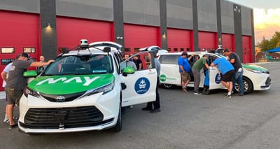 Two autonomous wheelchair vans parked outside of a garage.