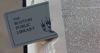 Boston Public Library card sticking out of a dictionary with the definition of the word library highlighted.