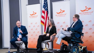 John seated on stage with two panelists at the All Wheels Up Global Forum.