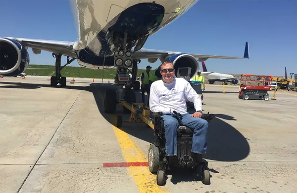 John seated in his wheelchair beneath a Delta Boeing 757 aircraft.