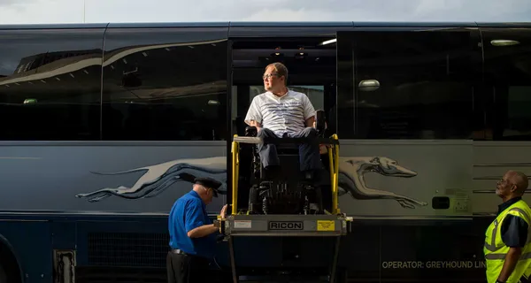 John Morris, seated in his wheelchair on the lift of a Greyhound Bus.