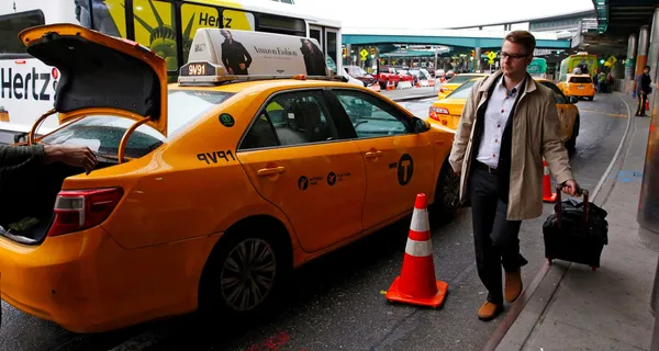 Man approaching taxi while pulling suitcase at airport cab stand.