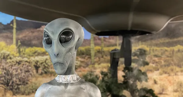 Close-up of an alien figure standing in front of a UFO in the New Mexico wilderness.