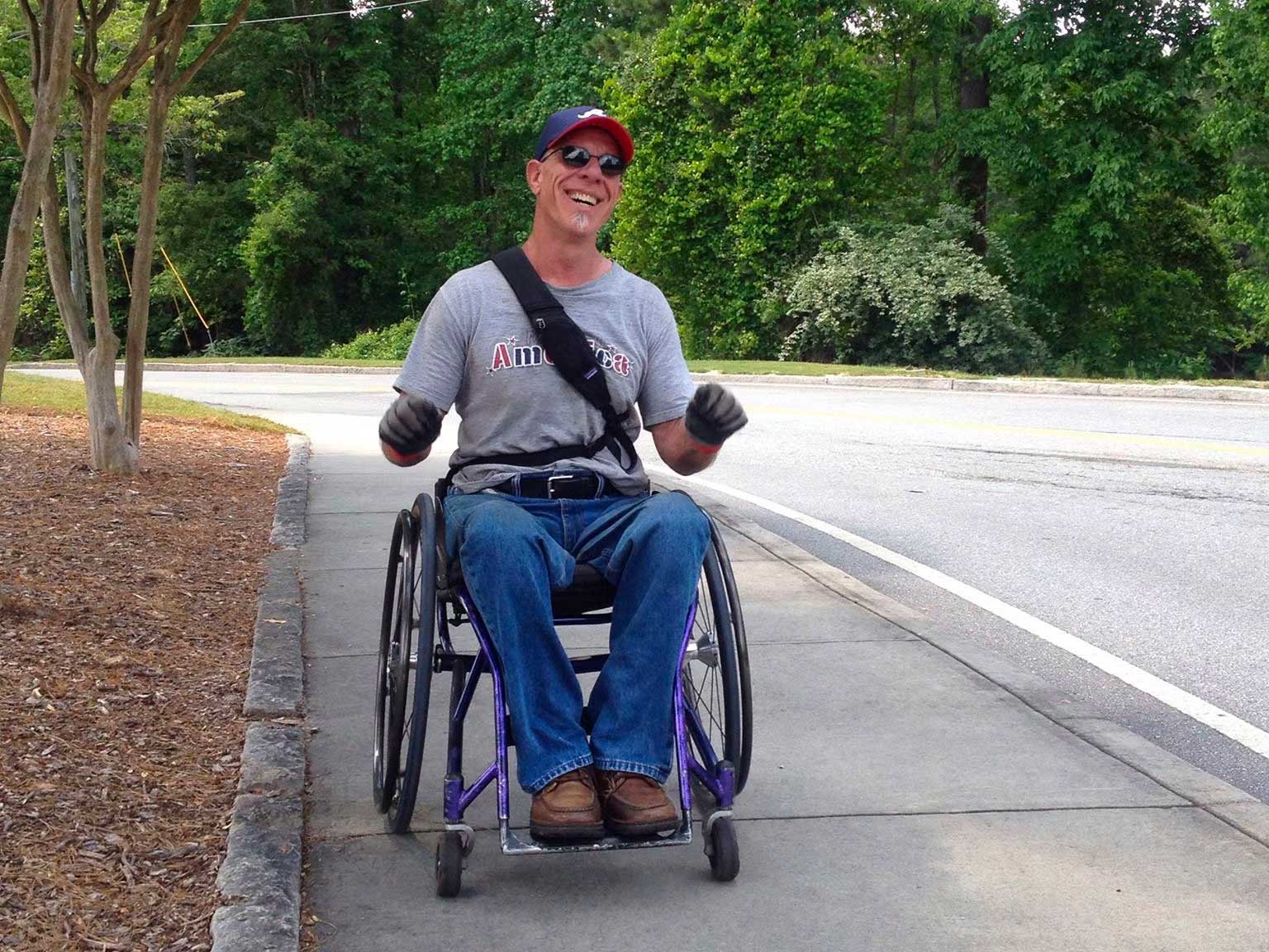 Man seated in a wheelchair on a sidewalk.